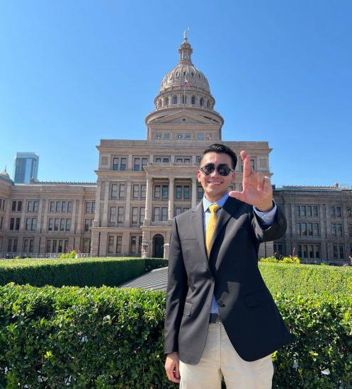 A person poses for a photo outside of a large government building.